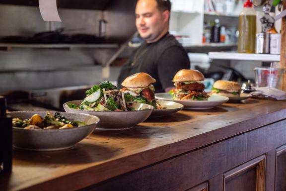 5 dishes from Raumati Social Club served on the bar, with the Chef standing behind.