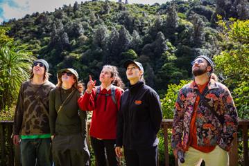 Four people and a Zelandia staff member stand beside one another looking up at the beautiful nature that surrounds them.