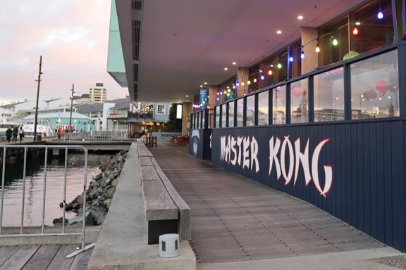 The exterior of Master Kong, a bar & restaurant on Wellington's waterfront during golden hour. There are colourful string lights and paper lanterns suspended above the patio. 