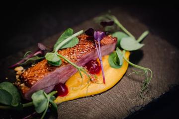 A close-up of a fine dining dish with a piece of fish, micro greens and an orange-coloured purée.