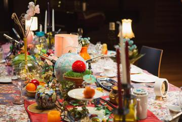 A big table filled with eclectic items like candelabras, oranges, vases, lamps and a globe.