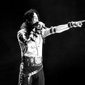 Michael Jackson, the king of pop, performed live. He's wearing a white jacket, holding a microphone to his mouth in one hand and pointing with the other. 