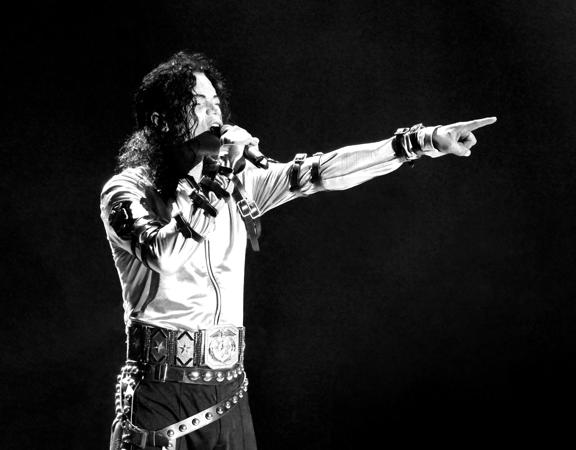 Michael Jackson, the king of pop, performed live. He's wearing a white jacket, holding a microphone to his mouth in one hand and pointing with the other. 