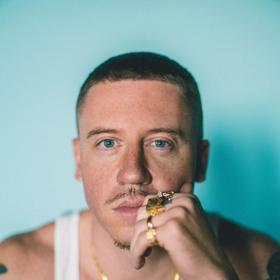 The rap-pop artist Macklemore stares directly at the camera in a close up of his face.