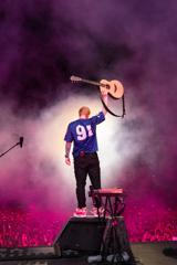 Ed Sheeran holds an acoustic guitar above his head during an applause break at one of his concerts.