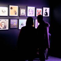 Three people look at The Art of Banksy exhibition in a dark room.