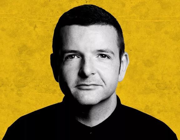 Headshot of Kevin Bridges in black and white on a grungy yellow background