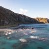 The rocky coastline, blue water, and mountains are at Red Rocks Coastal Walkway.