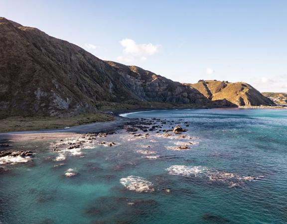 The rocky coastline, blue water, and mountains are at Red Rocks Coastal Walkway.