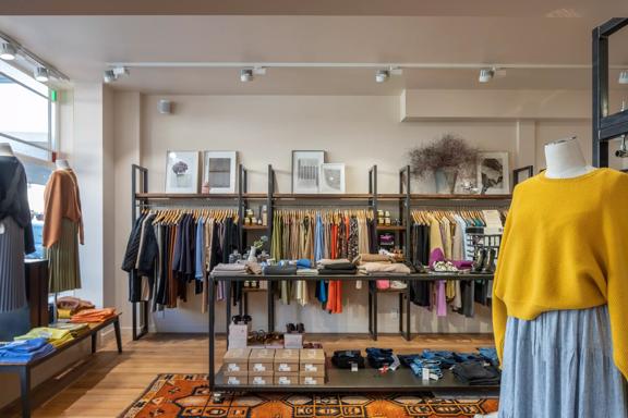 The interior of Goodness. Along the back wall are racks of clothing. In the middle sits a display of jumpers and shoes. And in the foreground, a mannequin wears a yellow jumper and denim skirt.
