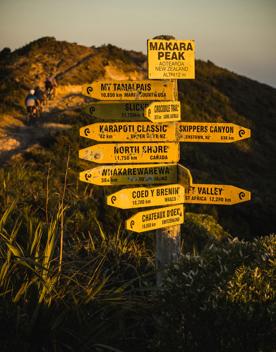 A yellow sign at the top of Mākara Peak mountain Bike Park showing other locations across the world and how far away they are.