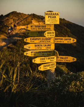 A yellow sign at the top of Mākara Peak mountain Bike Park showing other locations across the world and how far away they are.