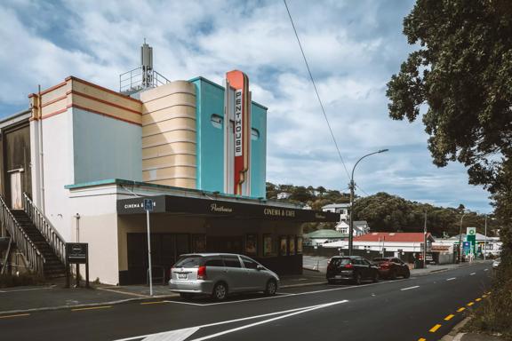 Penthouse Cinema & Cafe shown from the street looking towards the front of the building. The building is art deco style, with aqua, peach and red architectural detailing.