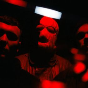 The three members of Kneecap pose in red light.