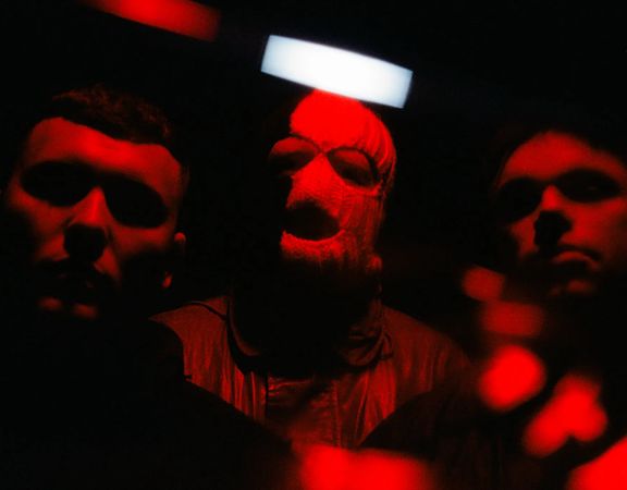 The three members of Kneecap pose in red light.