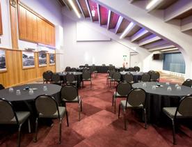 In the Norwood room at the Basin Reserve, circular tables covered in black tablecloths surrounded by chairs fill the space. On the left wall are wooden cricket rankings throughout the years.