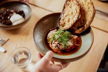 Close-up of a hand passing a breakfast dish called Istanbul eggs across the table at August Eatery in Wellington.