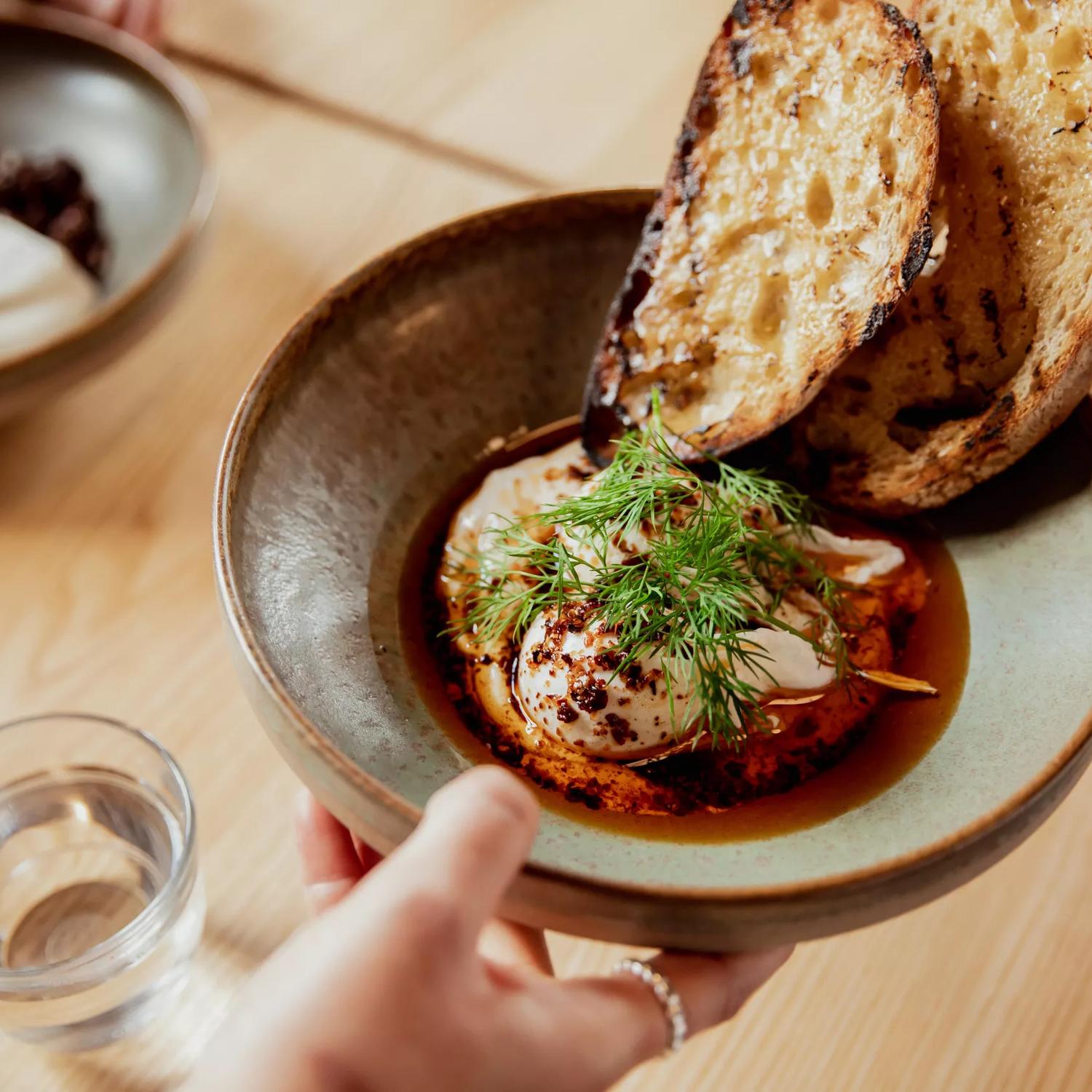 Close-up of a hand passing a breakfast dish called Istanbul eggs across the table at August Eatery in Wellington.