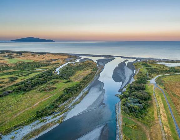 A drone shot of where the Ōtaki river meets the ocean, at sunset with Kapiti island in the distance.