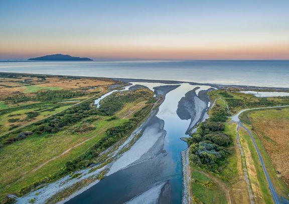 A drone shot of where the Ōtaki river meets the ocean, at sunset with Kapiti island in the distance.