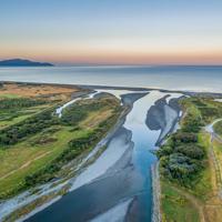 A drone shot of where the Ōtaki river meets the ocean, at sunset with Kapiti island in the distance.