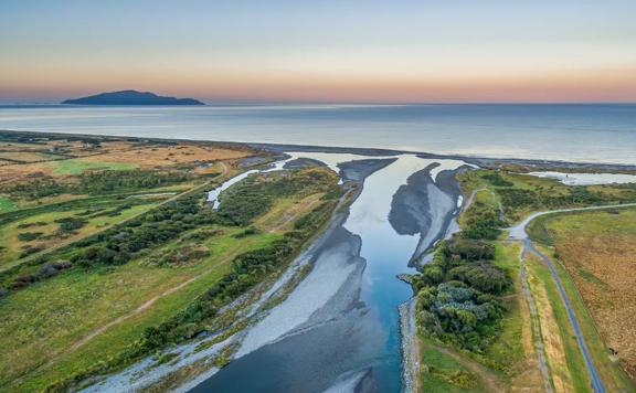 A drone shot of where the Ōtaki river meets the ocean, at sunset with Kapiti island in the distance.