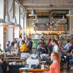 The busy and vibrant interior of Charley Noble, with customers sitting at tables and servers waiting tables, and kitchen staff in the background preparing food.