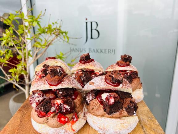 Five doughnuts sit, open-mouthed, on a wooden board. They're filled with chocolate cream, brownie pieces and strawberries.