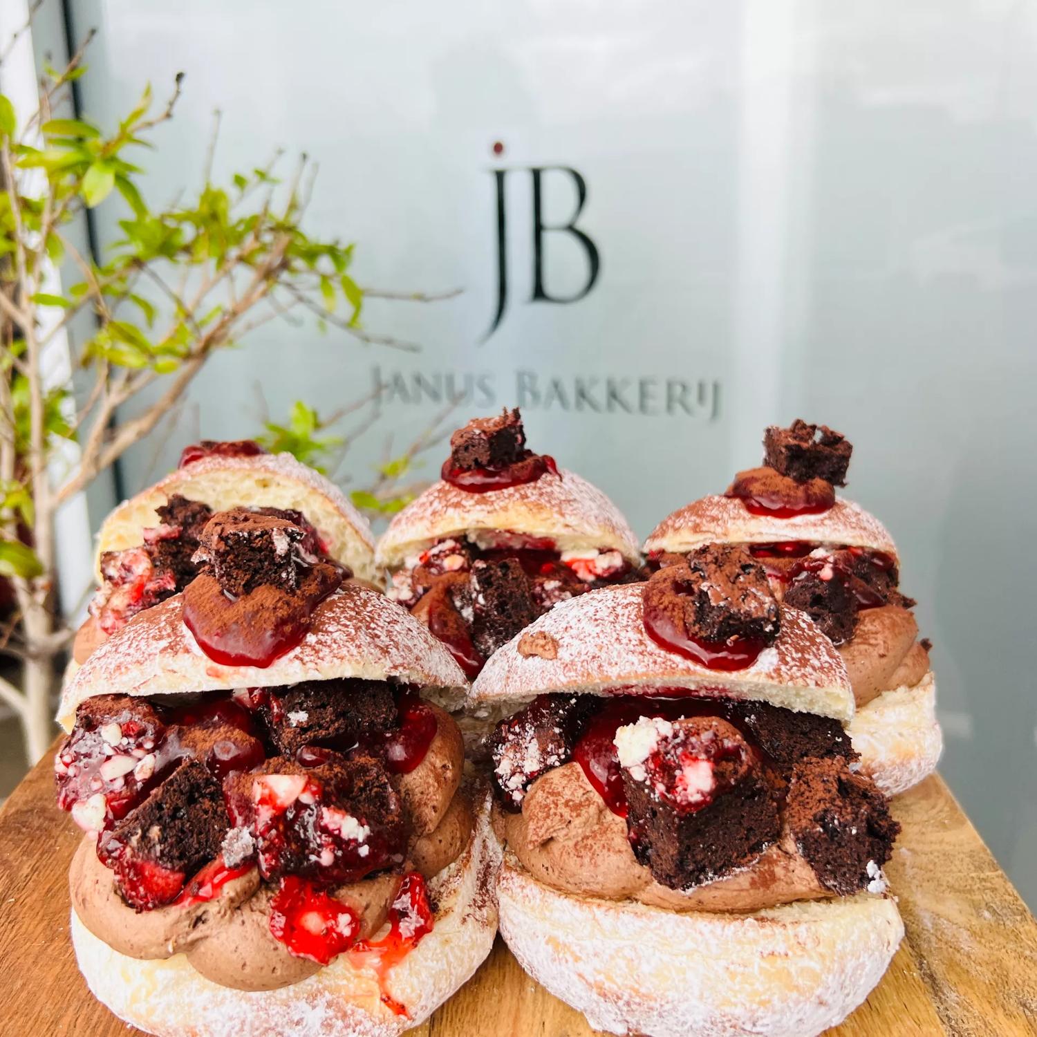 Five doughnuts sit, open-mouthed, on a wooden board. They're filled with chocolate cream, brownie pieces and strawberries.
