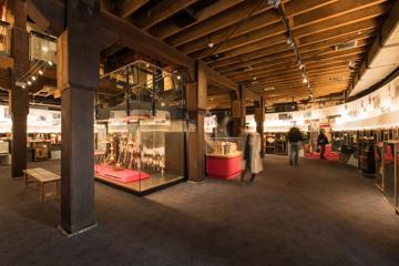 An exhibition room inside the Wellington Museum. Three people are walking and looking at the historical items on display.