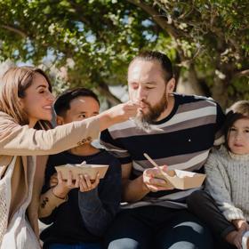 A family of four sitting together sharing some takeaway food outside.