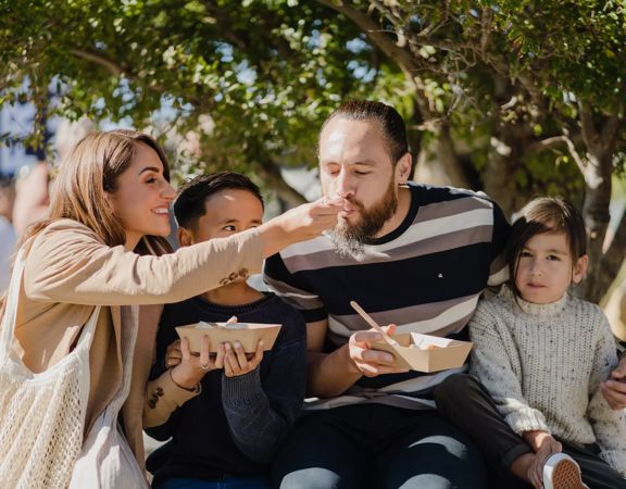 A family of four sitting together sharing some takeaway food outside.