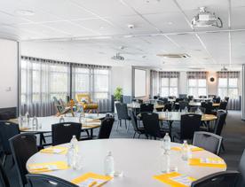 Conference room inside Atura Hotel, circular tables each with 6 chairs, notepads, pens and water.