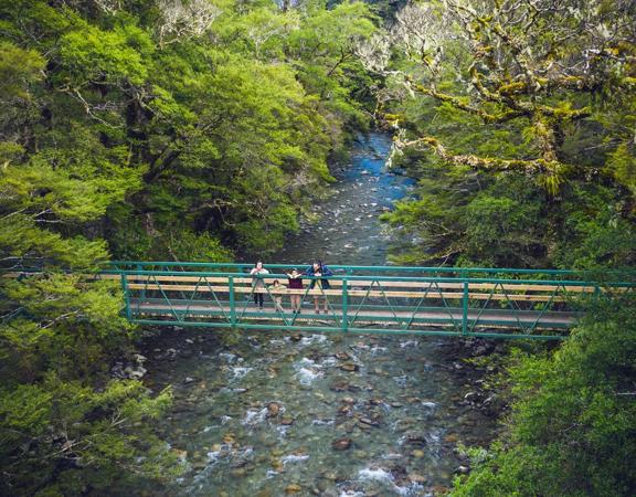 A drone shot of two adults and two kids standing on a bridge over a river in Tararua Forest Park.