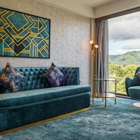 A room inside The Sebel in Hutt Valley, theresd a alrge couch and small chair both a velvet teal colour with gold accents.