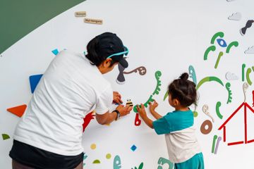 A child and a caregiver playing with stickers on a board at Capital E in Wellington