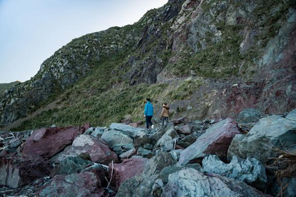 2 people walk along large rocks, on the Red Rocks Coastal Walkway.