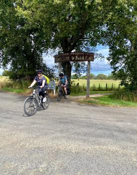 Two cyclists ride past the Greytown to Woodside Trail entrance sign.