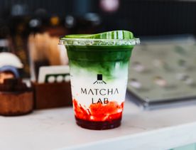 Iced matcha with strawberry puree in the bottom of the cup in a Matcha Lab branded takeaway cup.