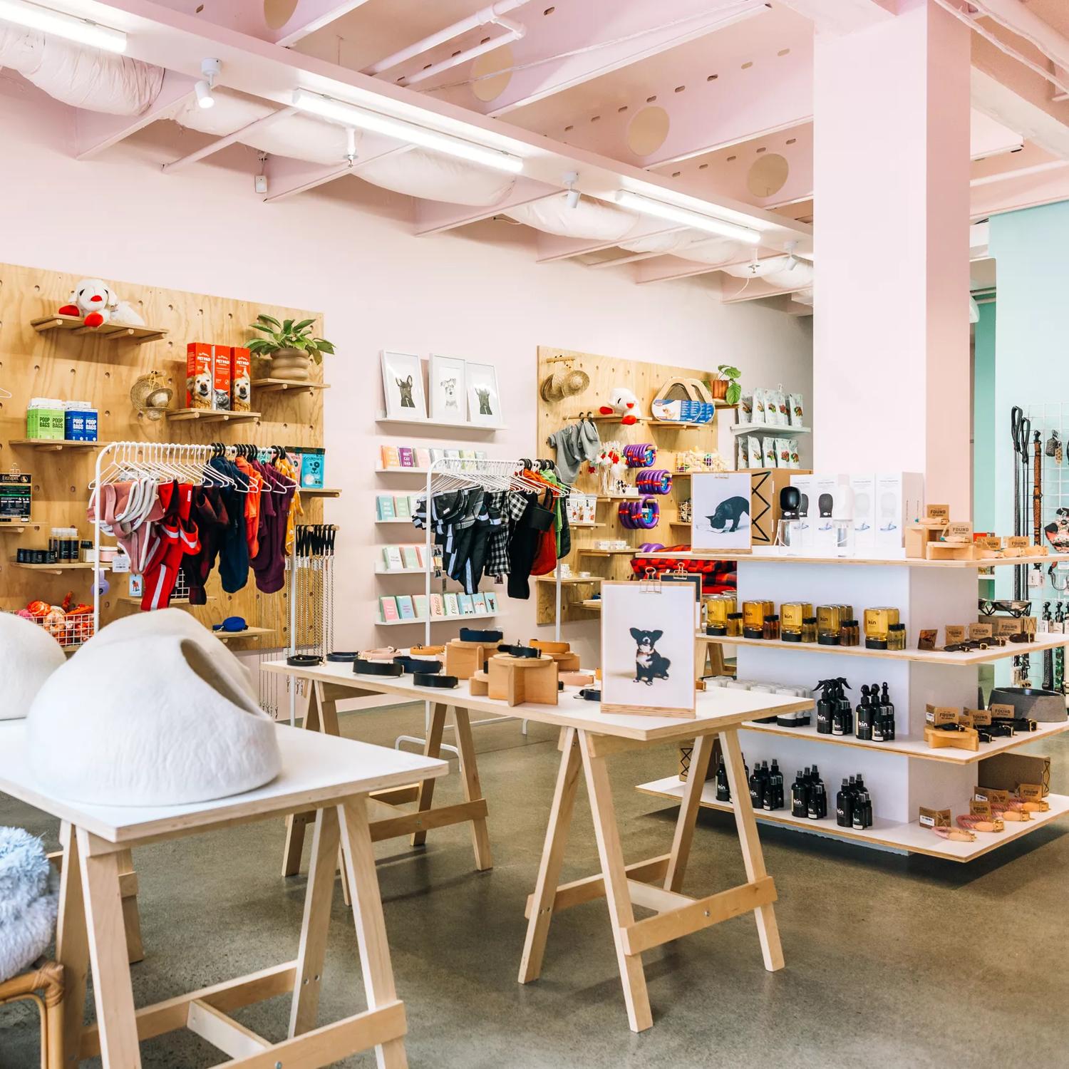 Interior image of Smack Bang. The walls are painted a soft pink. Trestle tables are in the foreground with pet merchandise on them. There are also shelves on the back wall full of products. 