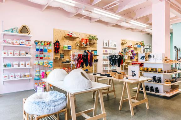 Interior image of Smack Bang. The walls are painted a soft pink. Trestle tables are in the foreground with pet merchandise on them. There are also shelves on the back wall full of products. 