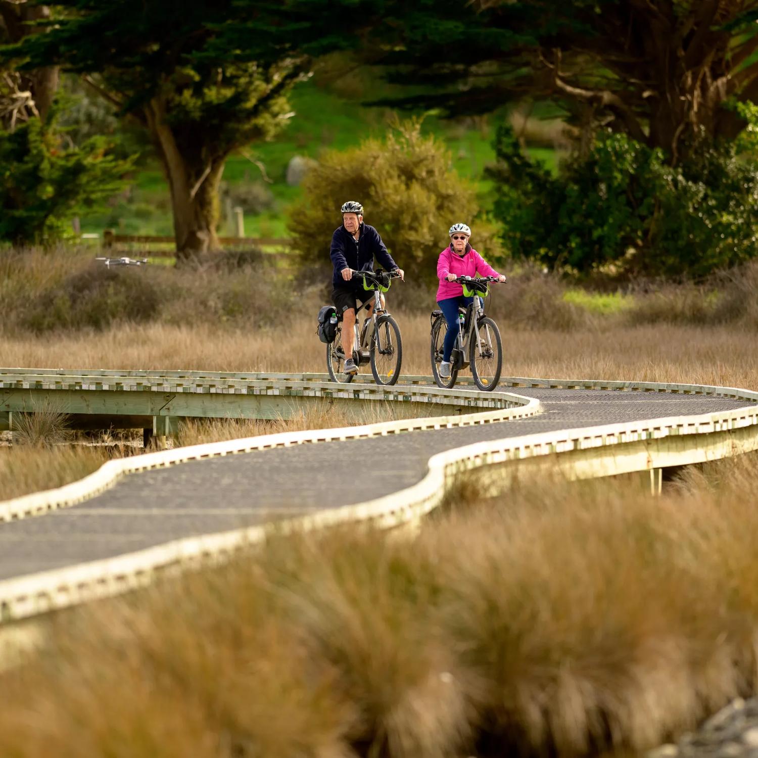 Two cyclists riding on an elevated wooden path in a nature reserve.