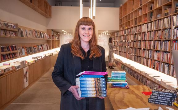 Manager and co-owner of Good Books Jane Arthur stands at the front of the store holding a stack of books.