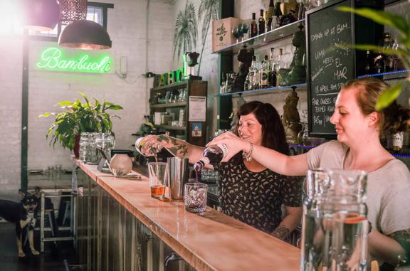 Two bartenders pouring drinks at the BambuchiSan bar, Green indoor plants occupy the background.