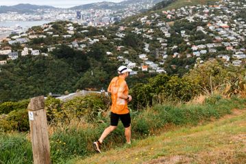 Trail runner mid-stride on a rugged forest track in Wellington, New Zealand, surrounded by native bush.