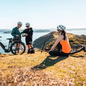3 people on bikes atop the hills on the Pencarrow coast, looking out into the Wellington harbour.