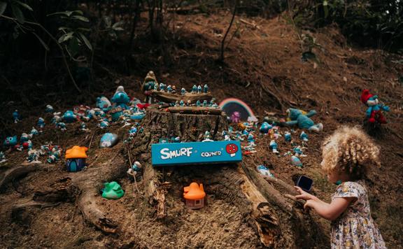 A child looks at a smurf-themed fairy village on the forest floor.