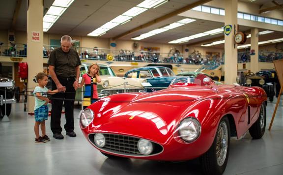 An adult and two children stand, looking at a red vintage convertible Ferrari in the Southward Car Museum in Otaihanga, Paraparaumu. 