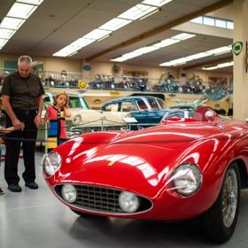An adult and two children stand, looking at a red vintage convertible Ferrari in the Southward Car Museum in Otaihanga, Paraparaumu. 