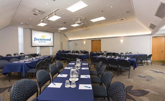 Side view of rectangle shaped room with 50 chairs around 8 tables facing towards a projector at the front of the room.